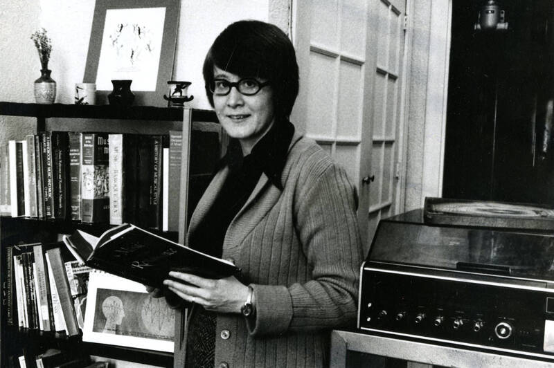 Former Mundelein administrator and teacher stands in front of bookshelf, holding an open book. 