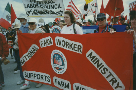 A group of people holding a banner and marching in support of farm workers. 